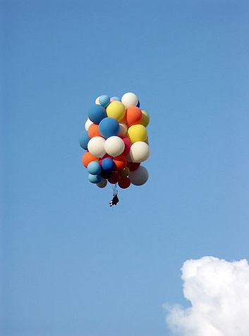 ein Himmel mit einer  Wolke.Ganz viele schwebende und zusammen gebundene Luftballons, an denen etwas hängt