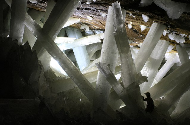 Eine Höhle mit einem wirrwarr von weissen dicken Stäben. Von der linken Seite ein Großer Lichteinfall. Rechts unten ist eine dunkle Gestalt zu erkennen.