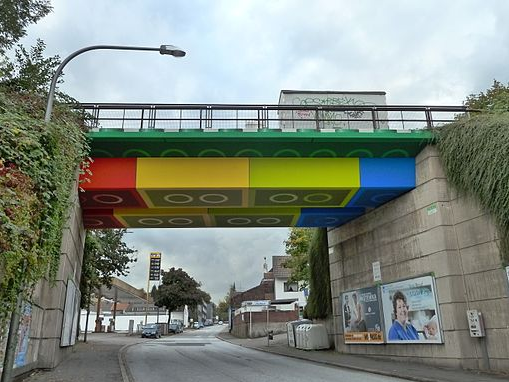 Strassenbrücke, deren Brückendach aus überdimensionalen Legosteinen besteht. Die Wände sind aus Beton.